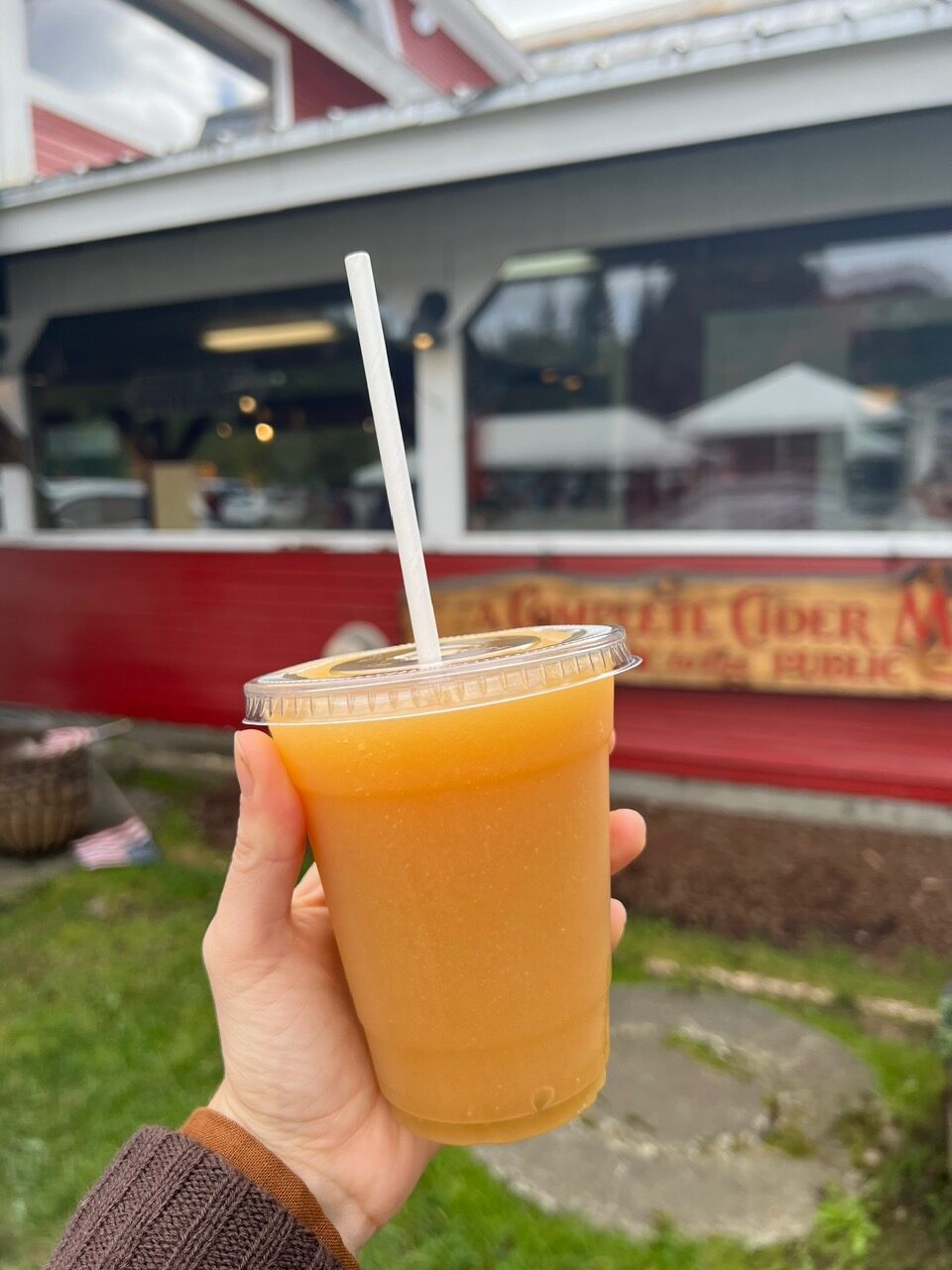 A hand holds a cold glass of cider, taken to go, from Cold Hollow Cider Mill. These fall-themed treats are so tasty! 