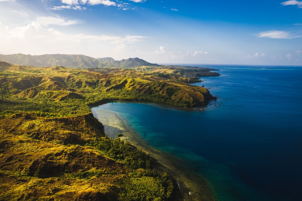 A stunning aerial view of a beach sunrise in Guam. The green island meets the sea.  