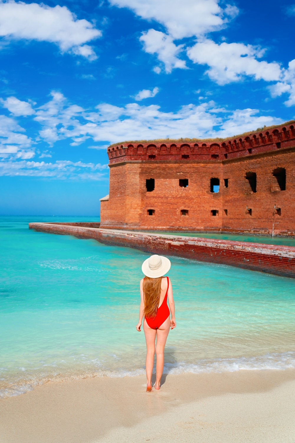 Women in red swimsuit and a white hat stood by the water with the font in front of her.  Dry Tortugas National Park