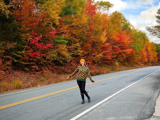 woman standing on a fall foliage lined road