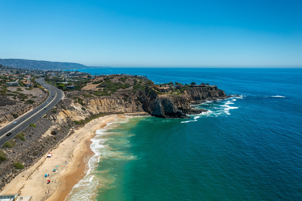 An arial shot of the coast of California shows why this is one of the prettiest states in the USA: the blue waters froth against tan shores and the rocky cliffs and mountains are so close to the highway, offering great views. 