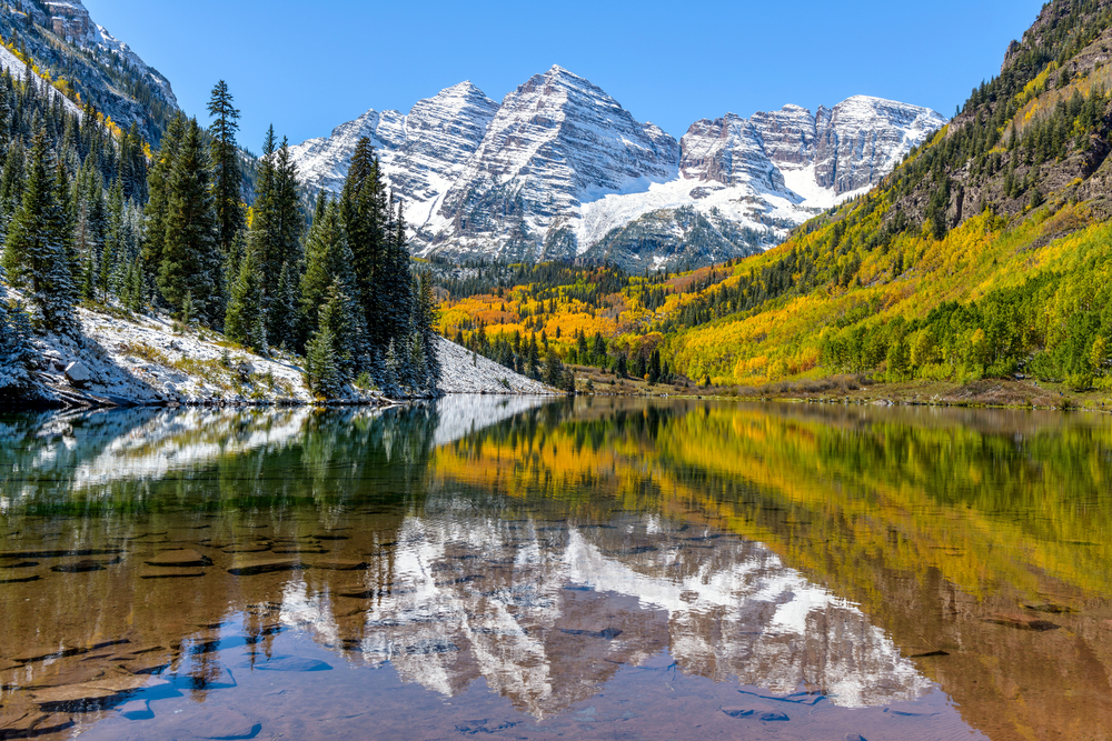 Snowcapped mountains hover over lines of trees that slope down into crystal clear water. In the water you can see the reflection of the mountains: no wonder Colorado is one of the prettiest states in the USA. 