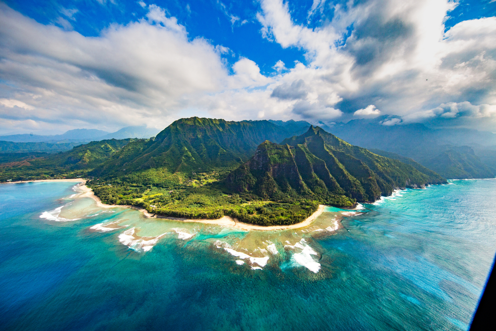 Hawaii is without a doubt one of the prettiest states in the USA as seen in this photo with its massive mountains that are green and sharp, and with its white sand and blue, frothy waters. 