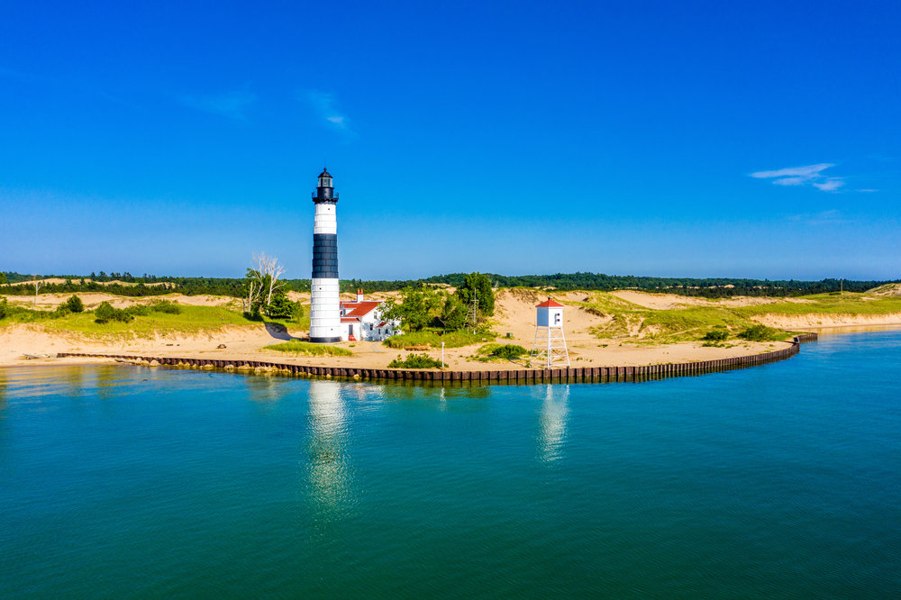 Michigan is one of the prettiest states in the USA: this photo shows one of the Great Lakes and its calm, blue water, with its sandy shores and a black and white traditional lighthouse on the cusp. 