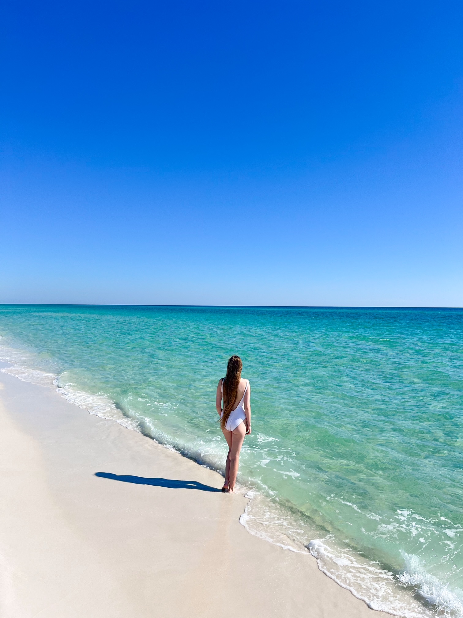 a girl in white swimsuit standing in from of the beach with turquoise waters