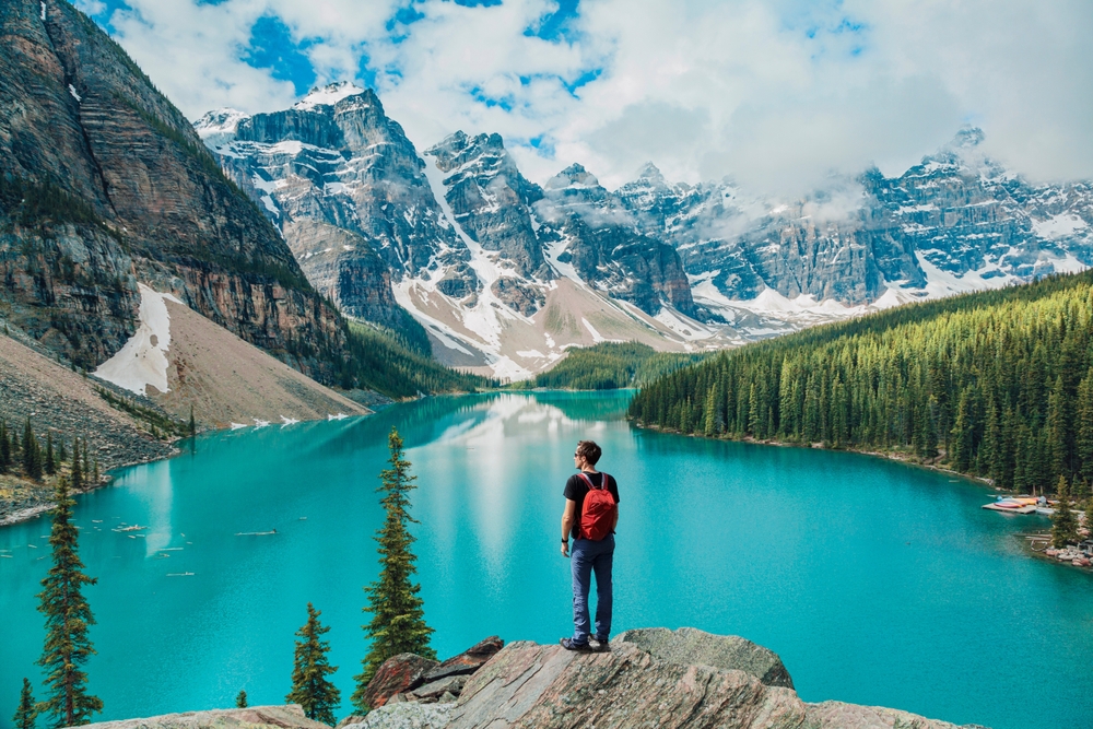 A man standing on a cliff edge over looking Morraine Lake in Banff National Park in Canada, one of the best 30th birthday travel ideas for him.