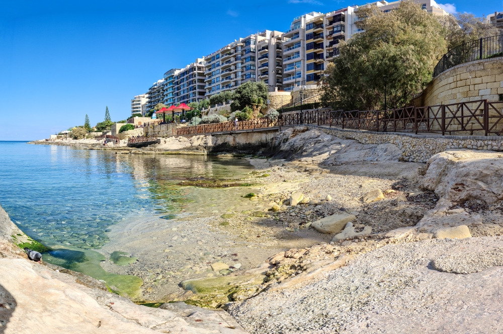 a beach in malta, wall buildings line the water on a clear sky day in november, one of the best places to visit in europe in november 