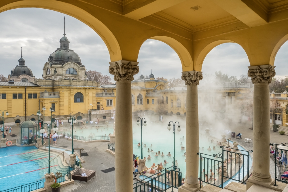 there are thermal baths visible through archways in Budapest, there are people in the baths