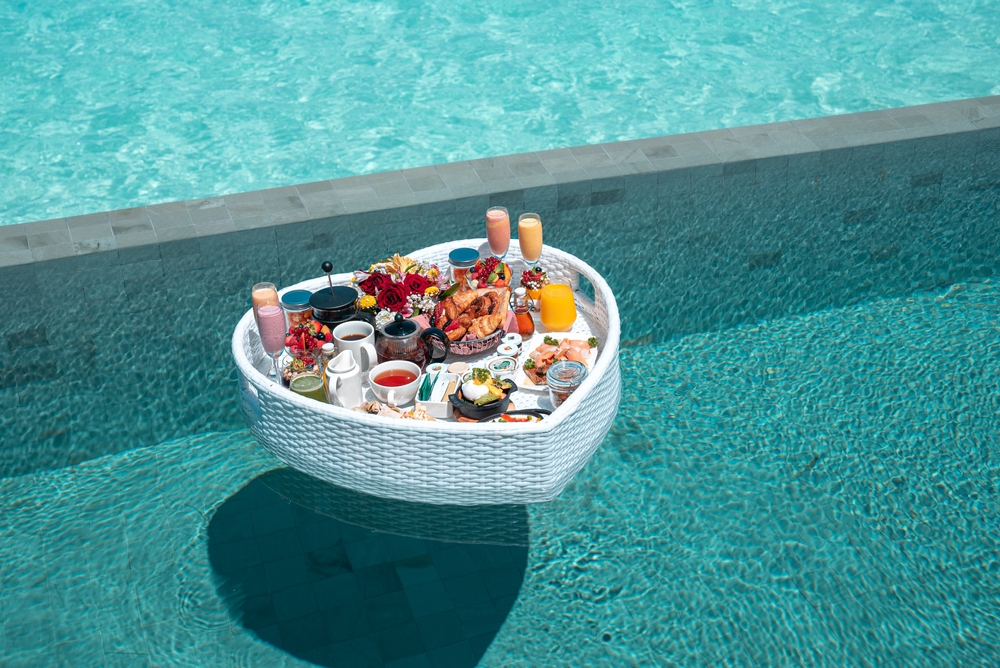 Breakfast in swimming pool, floating breakfast in heart tray tropical resort. Table relaxing in calm pool water, healthy breakfast and fruit plate by resort pool in Maldives. Article is about the best time to visit the Maldives