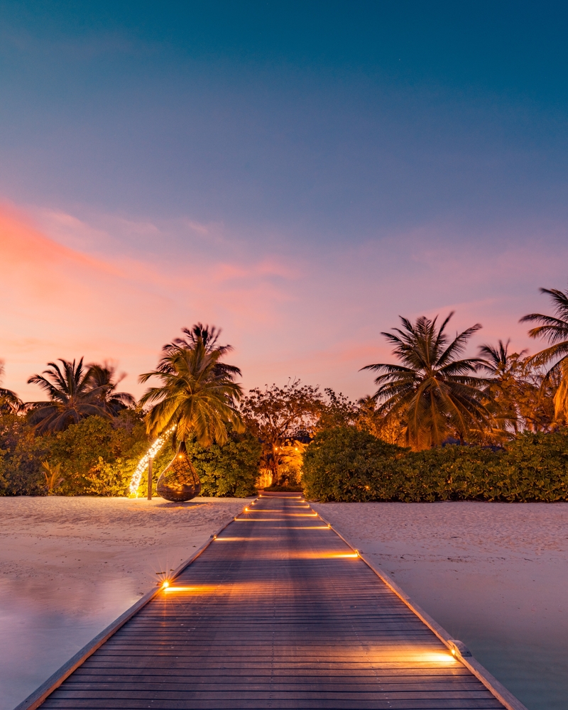 Amazing sunset panorama at Maldives. Luxury resort villas seascape with soft led lights under colorful sky. Article is about the best time to visit the Maldives. 