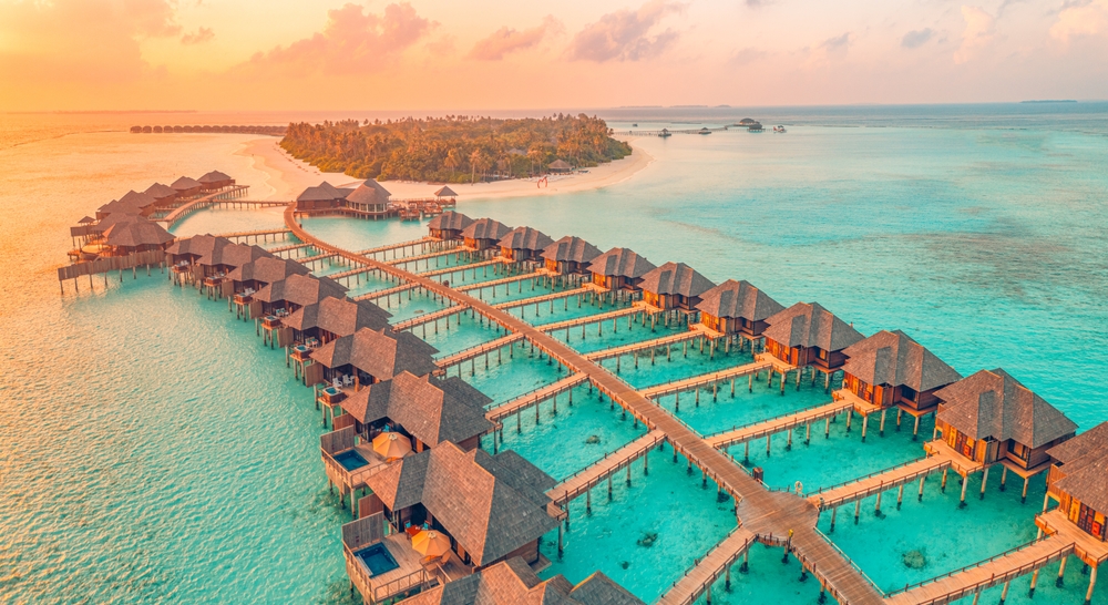 Aerial sunset panoramic landscape luxury tropical resort water villas. Beautiful island beach orange sunrise sea sky.