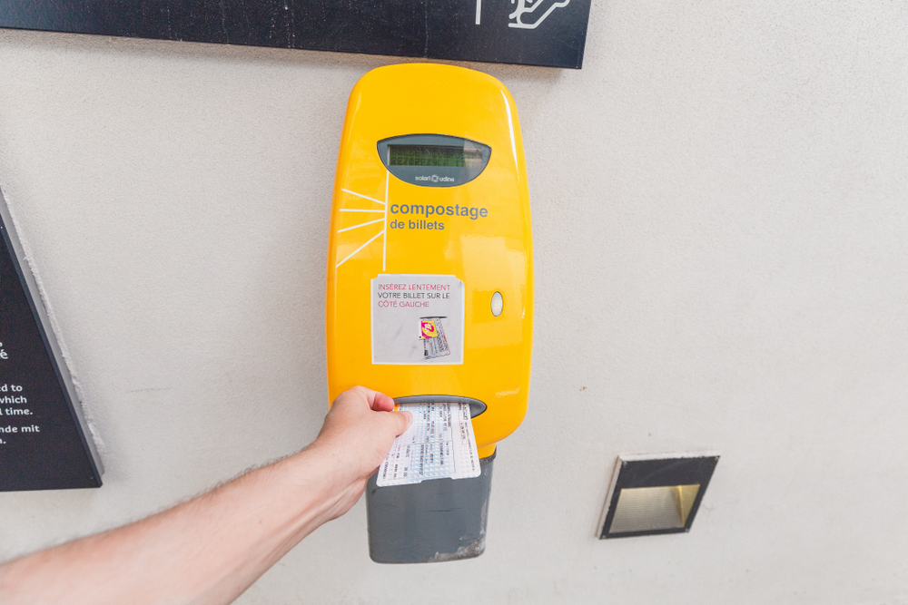 A hand reaches forward the validate their tickets at a French train station. The yellow compostage stamps a ticket, and not validating tickets is one of those mistakes to avoid in Europe. 