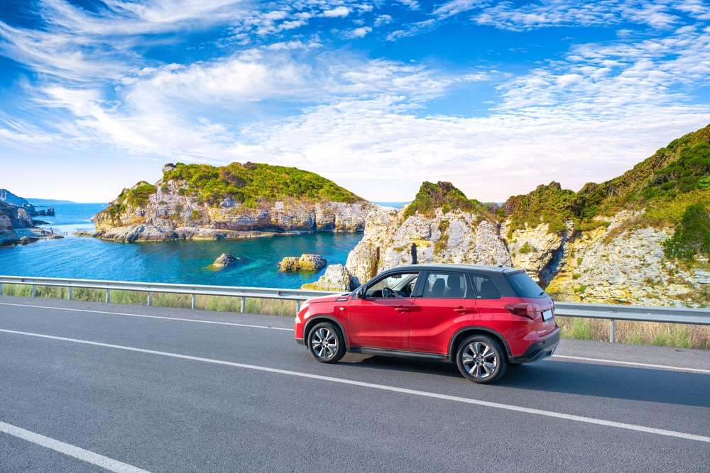 A red car hugs the coast of a highway in Italy, with rocky coasts and blue waters: this drive isn't afraid of driving, which is mistakes to avoid in Europe.