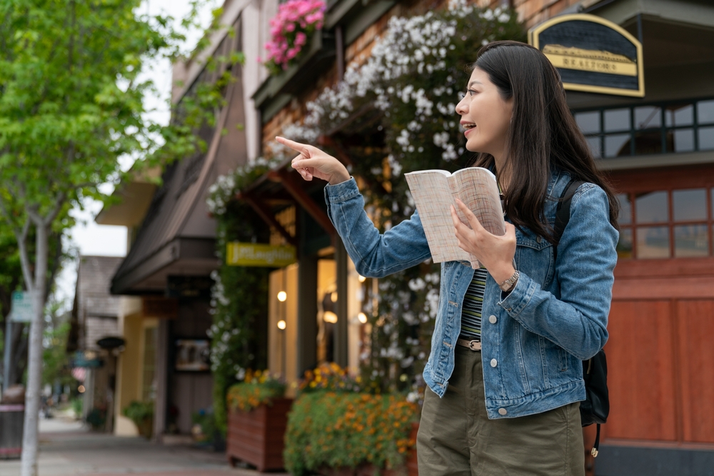 A young woman gets caught up in her guide book, doing too much research, which is one of the mistakes to avoid in Europe. She points across the street at something but missing the beautiful, historic pubs behind her. 