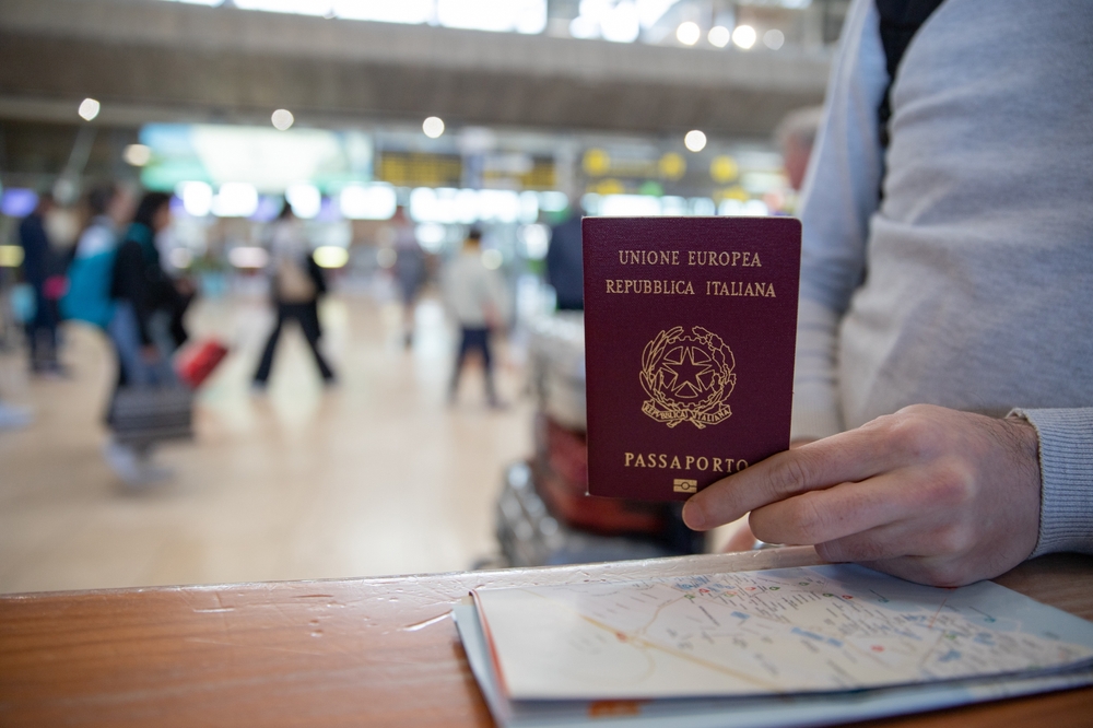 A hand holds and Italian passport, which is red in color with gold writing, at customs in the airport: having copies of documents like this is vital, and one of those mistakes to avoid in Europe. 