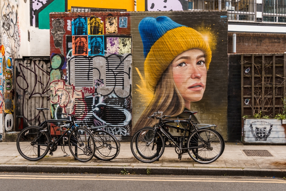 Bicycles parked on Redchurch Street in Shoreditch. The wall is covered in a large picture of a girl. 