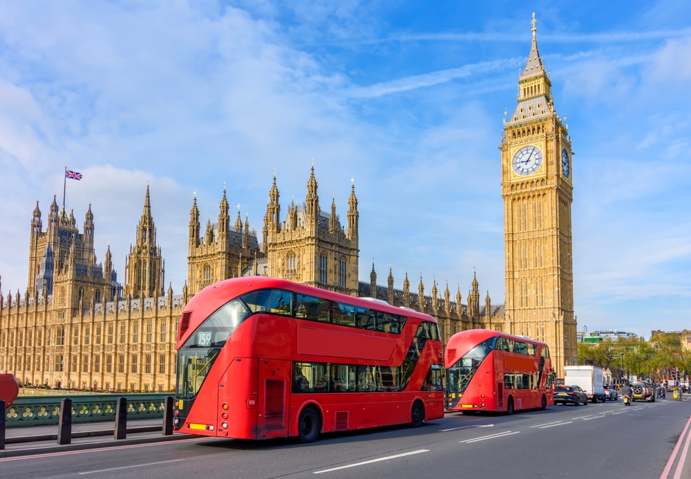 Houses of Parliament with Big Ben and double-decker buses on Westminster bridge, London, UK. The article is about mistakes to avoid in London. 