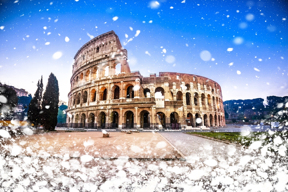 Snow flurries around an empty Colosseum  in Rome, the sky blue and purple beyond the famous landmark. 