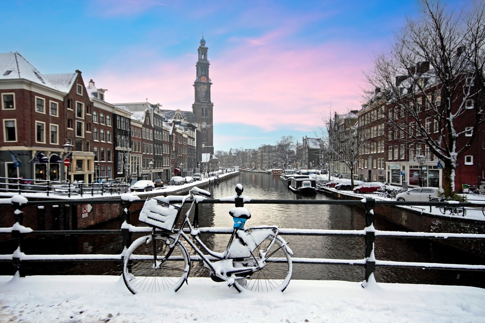 A bike leans up against a railing on the bridge in Amsterdam, coated in snow. The surrounding streets have layers of snow during this winter season! 