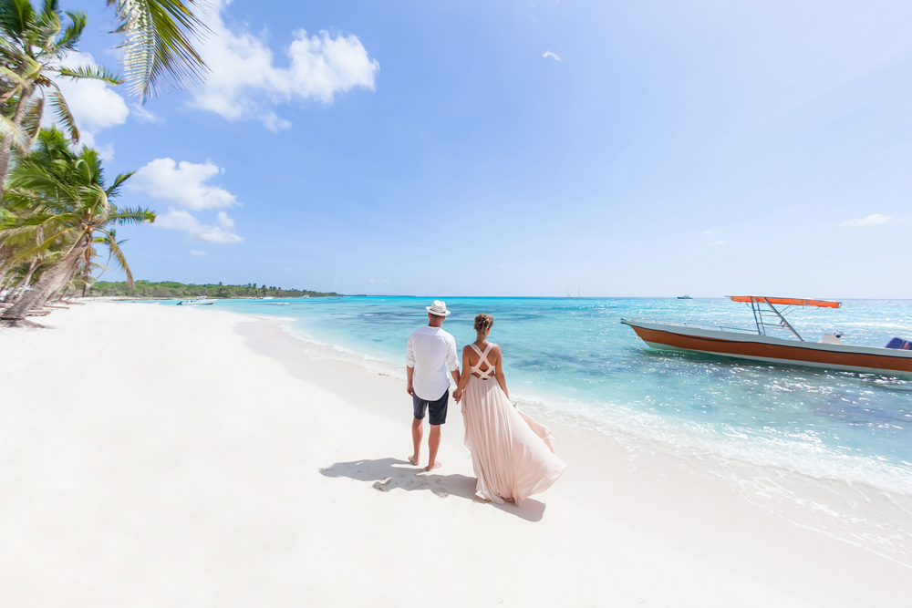 a couple on the white sand beach holding hands about to get on a boat in the stunning Caribbean waters