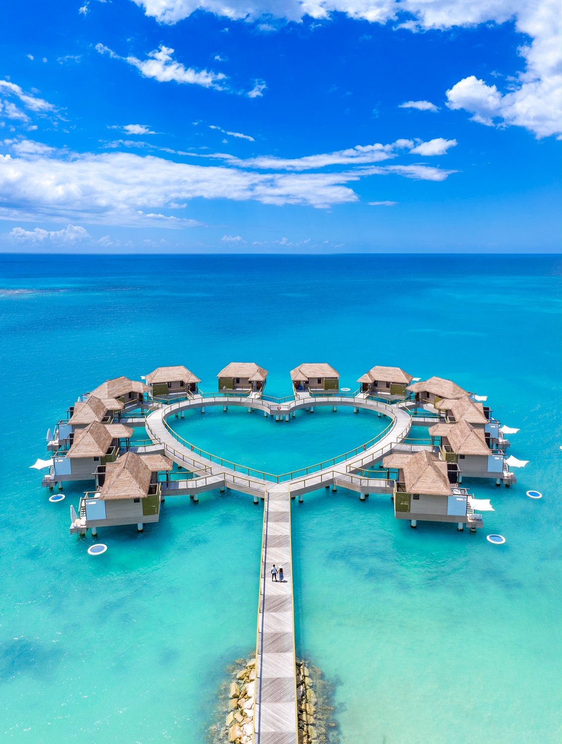 a heart shaped bungalows at the Sandals South Coast in Jamaica one of th best all inclusive Caribbean honeymoon resorts with a couple standing on the wooden boardwalk