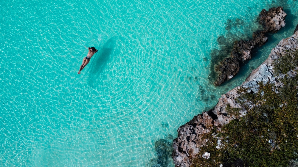 a woman sunbathing in a glass bottom kayak in the turquoise water and surrounding cliffs in Turks and Caicos one of the Caribbean honeymoon destinations