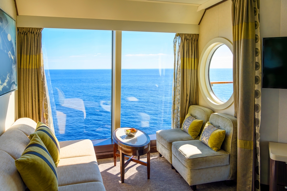 The tiny room of a cruise is just that: a room that features space for sleeping and getting change to go explore the rest of the ship! This view has a giant window and two couches. 