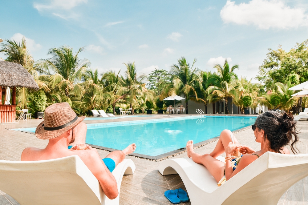 When considering  all inclusives vs cruises, debate what is best fit for you: in this photo a couple lays out by the pool, drinks in hands. 