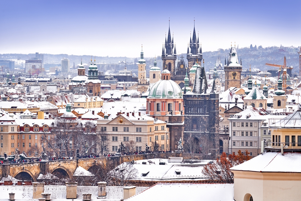 photo. of snow covered buildings in january, there are two tall spires in the background, and a domed building in the middle of the image 