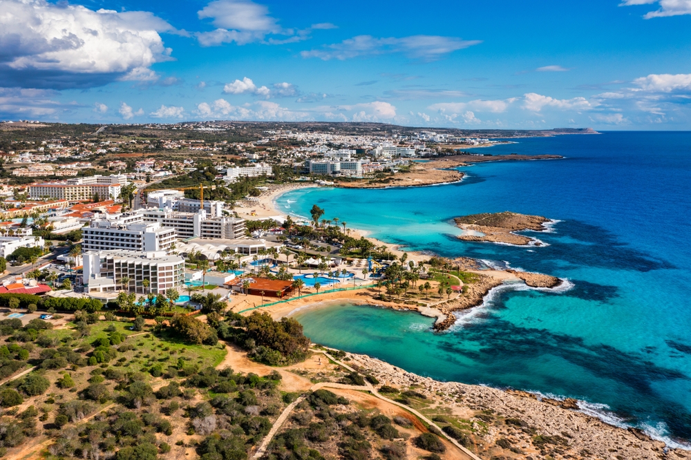 curved coastline, buildings on land on the left and the transparent blue water is on the right 