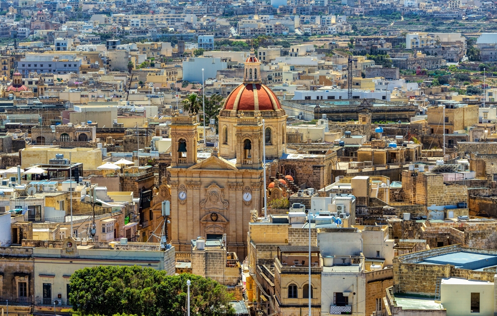 aerial photo of gozo, malta, there is a domed building in the middle of the image, some trees are peeking through between buildings