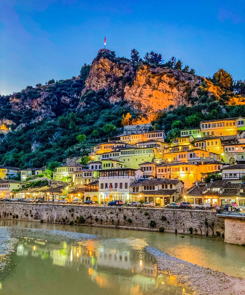 The 1000 windows of iconic Berat Albania. The evening lights from the city reflect on river and the houses are painted green, yellow and orange. The blue hour highlights Berat Castle on the mountain.