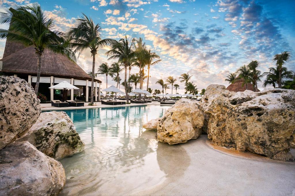 Outside swimming pool surrounded by rocks, palm trees and loungers. 