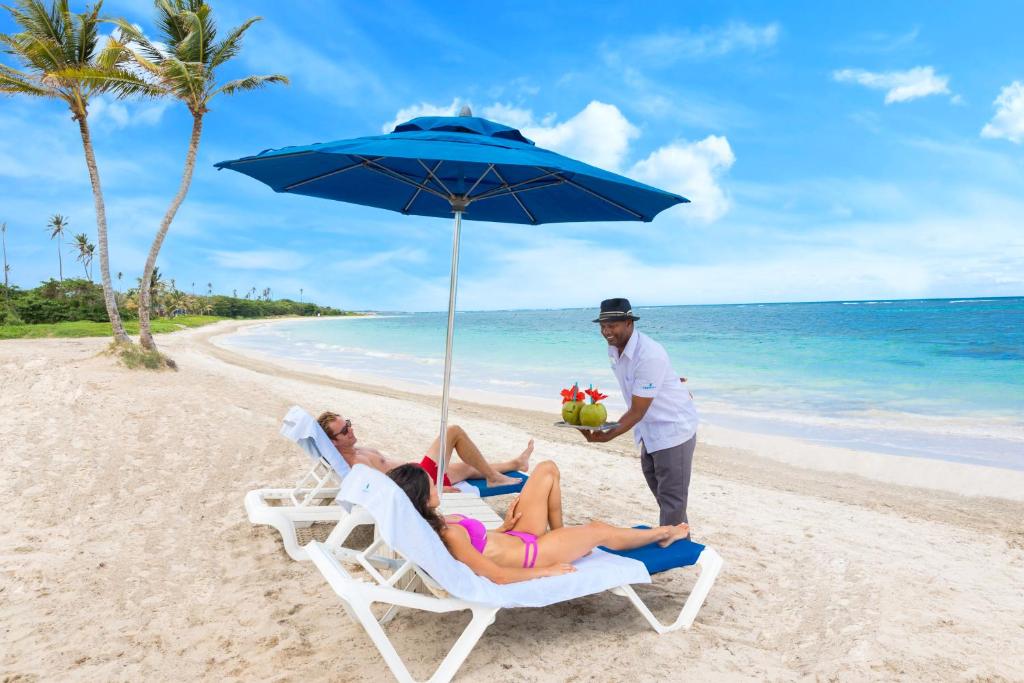 male and female on loungers on the beach been served cocktails. 