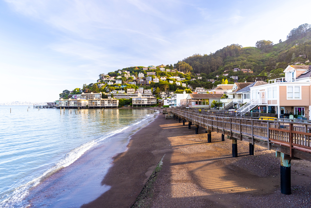 in the distance, homes are built into a hill overlooking the water, with an elevated walkway along the shoreline in the foreground in Sausalito, California