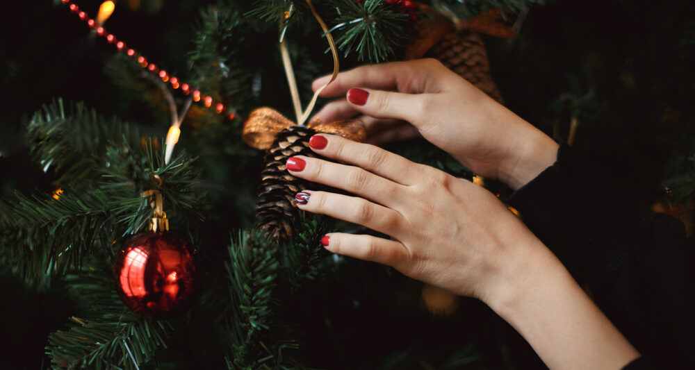 woman hanging ornament on a tree showcasing a christmas manicure