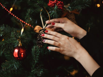 woman hanging ornament on a tree showcasing a christmas manicure