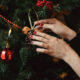 woman hanging ornament on a tree showcasing a christmas manicure