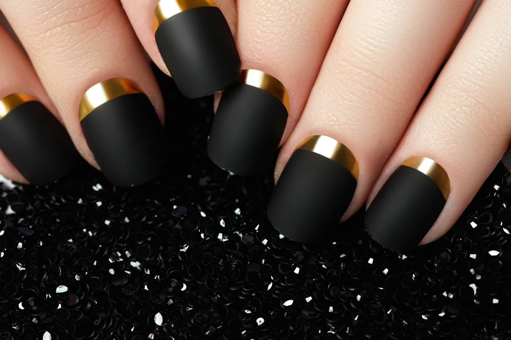 Manicured nail with black matte nail polish. Manicure with dark nailpolish. Golden nail art manicure