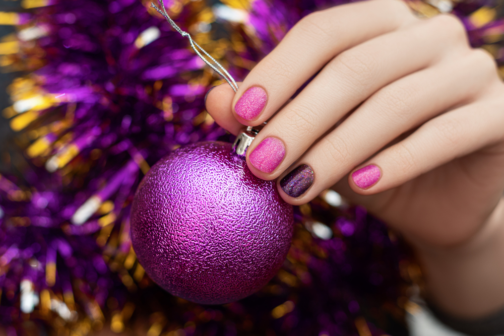 Woman hand with Christmas and New Year nail design hold glittering toy decoration.