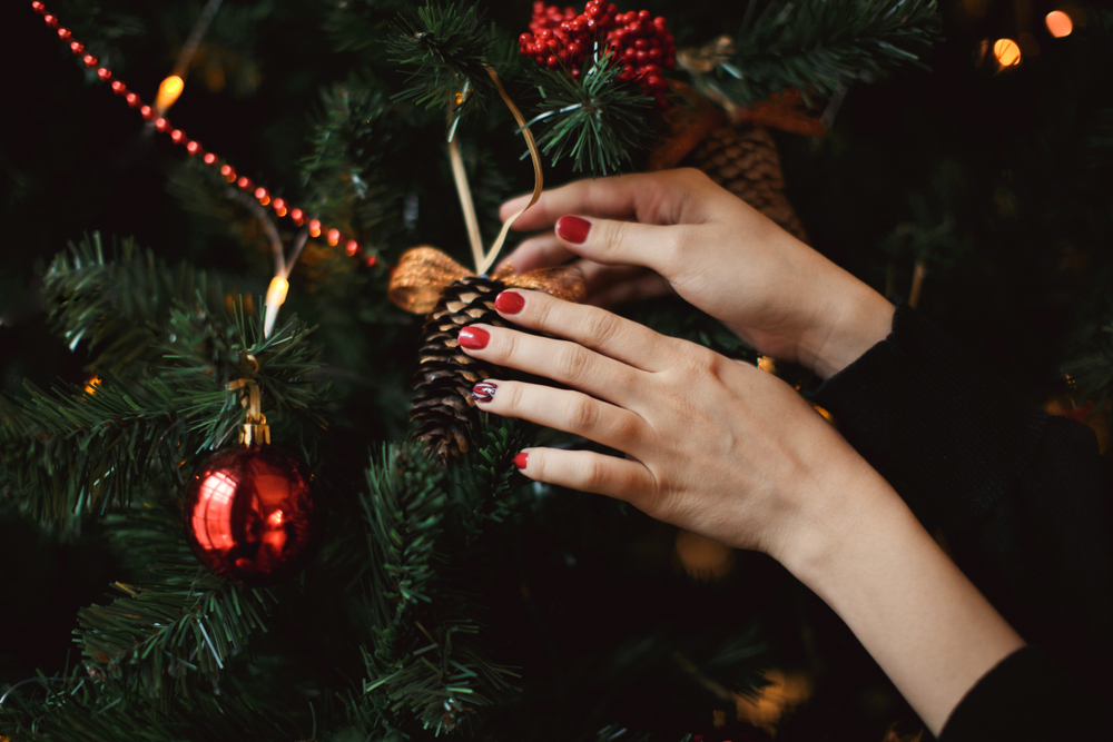 Female hands with a red manicure. Christmas composition with balls and lights. The article is about Festive Christmas Nail Ideas for winter travel. 