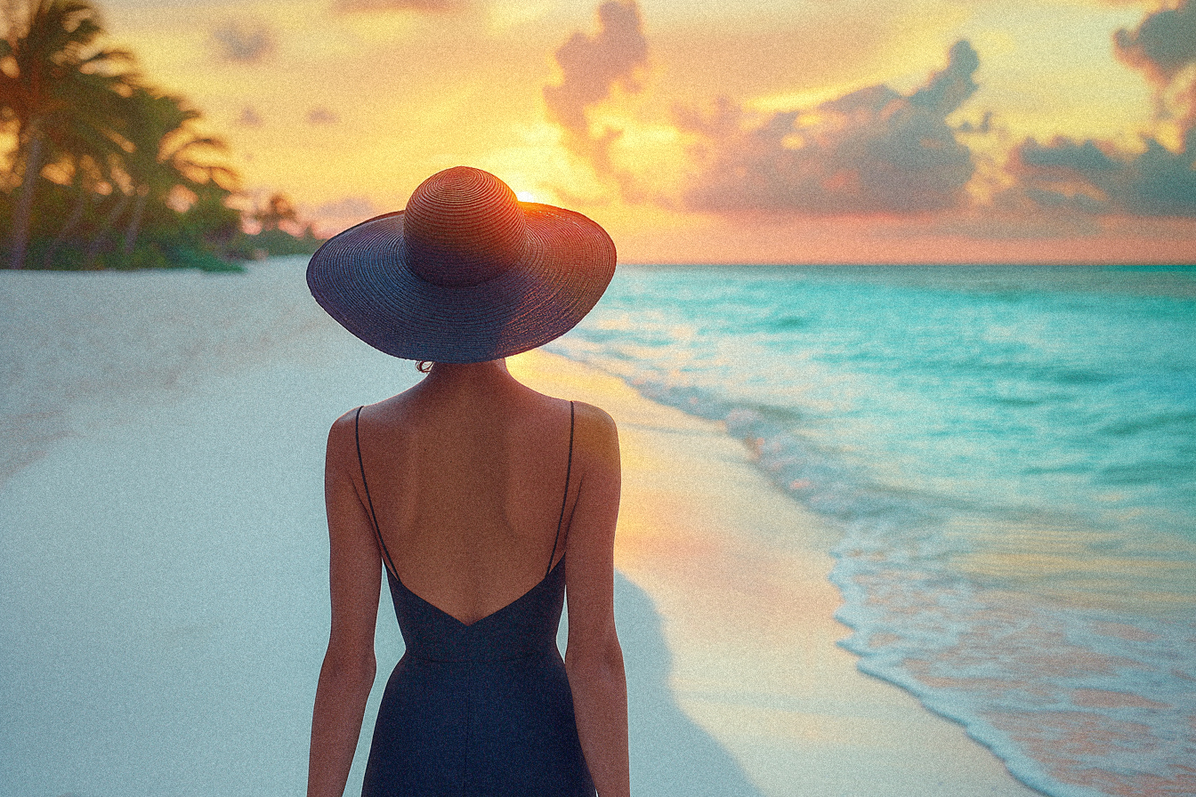 A woman gazes out at a beach during sunset, wearing a black spaghetti-strap dress and a wide-brimmed black hat. The simple, elegant outfit contrasts beautifully with the soft colors of the ocean and sky, evoking a sense of calm and sophistication.