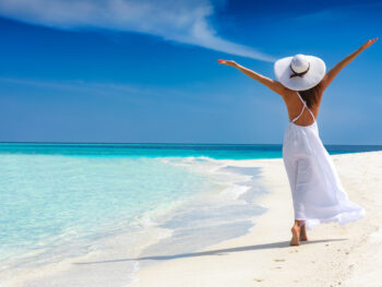 woman standing in white dress with her hands in the air as she walks along the beach