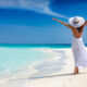 woman standing in white dress with her hands in the air as she walks along the beach