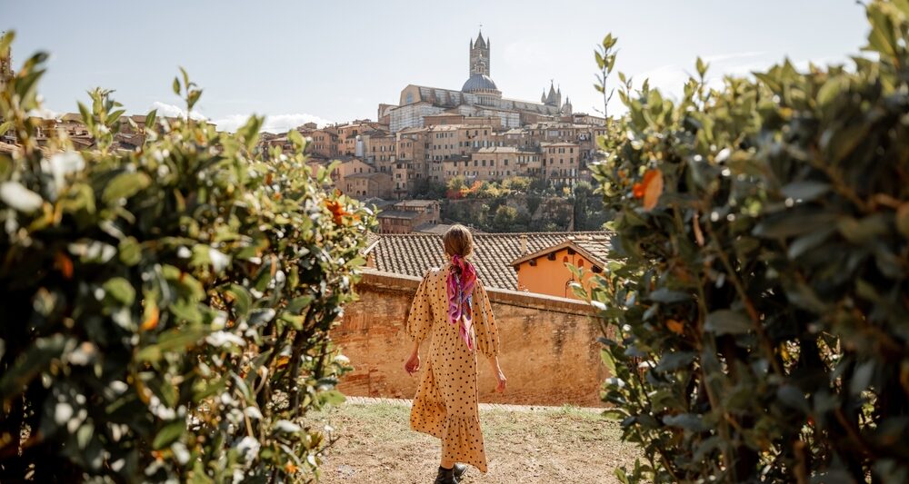 woman standing in tuscany italy wearing a brown dress surrounded by vineyards