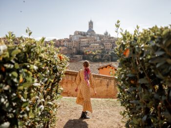 woman standing in tuscany italy wearing a brown dress surrounded by vineyards