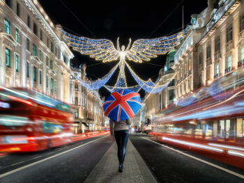 woman standing with a british flag umbrella on the streets of london in december