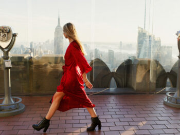 woman wearing a red dress walking with NYC skyline in the background