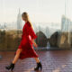 woman wearing a red dress walking with NYC skyline in the background