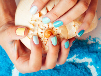 woman wearing nailpolish painted for the beach holding a shell